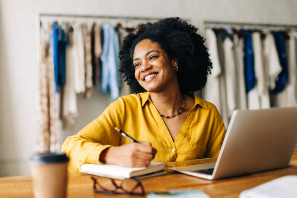 istock Happy fashion designer writing ideas for her small business in a note book 1742458320