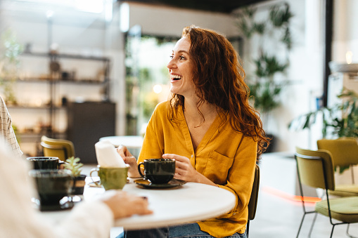 Woman catching up with friends over coffee in a restaurant, chatting and enjoying the lively atmosphere. Happy young, Caucasian woman socializing with a group of people in a cafe.