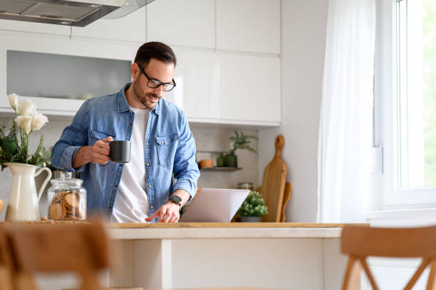 istock Focused businessman holding coffee cup and reading e-mails over laptop on kitchen counter at home 1742479447
