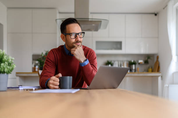 istock Handsome entrepreneur with coffee cup and laptop on desk thinking ideas while sitting at home 1742479987