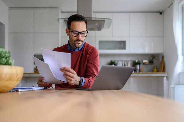 istock Serious financial advisor holding financial reports and using laptop on desk while working from home 1742479988