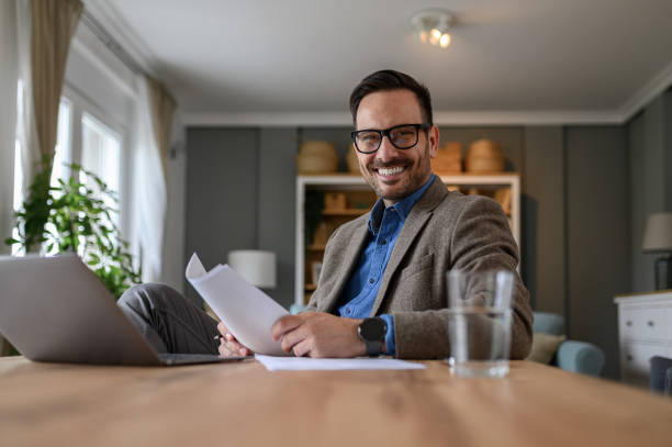istock Smiling elegant businessman holding documents and looking at camera while working from home 1742480602