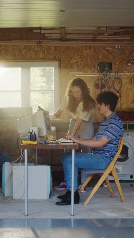 Vertical Screen: Caucasian Male Software Developer And Hispanic Female Designer Talking And Using Old Desktop Computer in Retro Garage. Diverse Startup Founders Working On Online Service In Nineties.