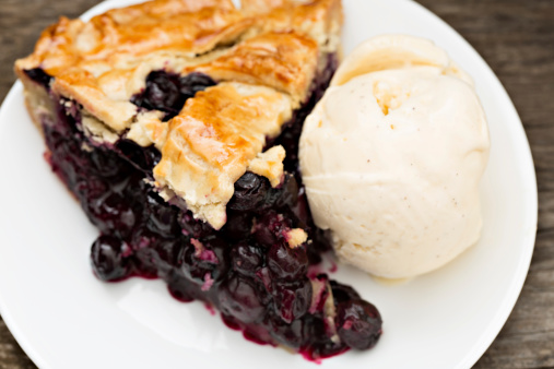 A high angle close up shot of a slice of freshly baked blueberry pie with a scoop of french vanilla ice cream.