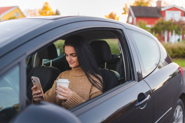 istock Beautiful young woman sitting in a car while using her phone and drinking coffee 1742504377