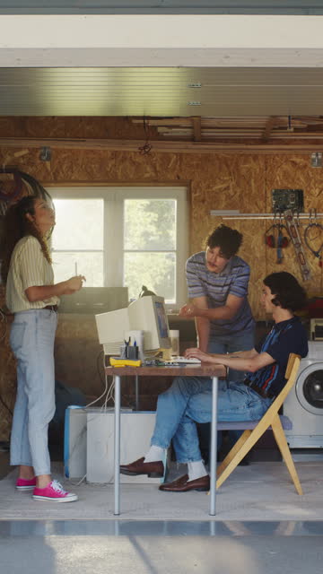 Vertical Screen: Diverse Team Of Three Young Tech Startup Company Founders Working In Retro Garage, Using Old Desktop Computer. Male And Female Entrepreneurs Developing Online Service In Nineties.