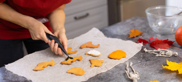 istock A girl pours bat-shaped cookies with black Halloween icing. 1742516618