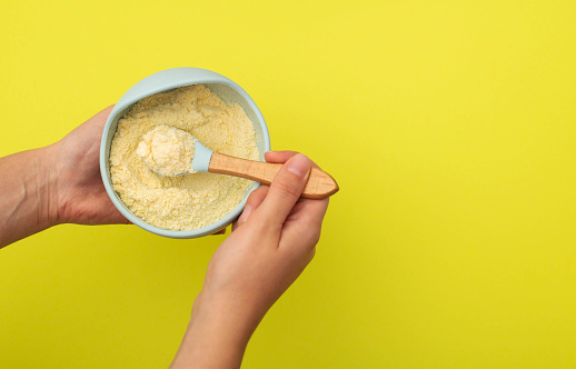 mother in her hands holds a plate with dry dairy-free wheat porridge with pumpkin for her baby on a yellow background. Concept of feeding vitamins and minerals to a baby