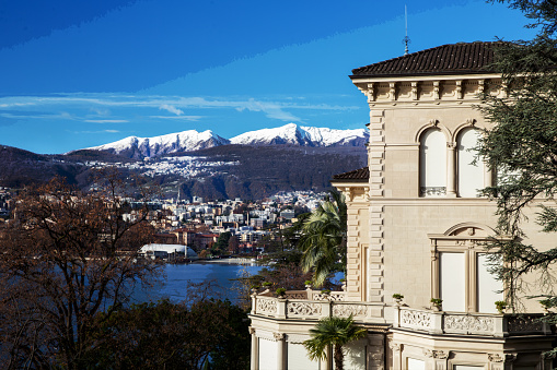 Awe sunny landscape with  part of old villa in Lugano suburb and Lugano city and Swiss Alps - fantstic snowcapped mountains in  winter