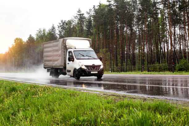 A small truck transports cargo against the backdrop of a forest on a wet road in the rain, industry A small truck transports cargo against the backdrop of a forest on a wet road in the rain truck in rain stock pictures, royalty-free photos & images
