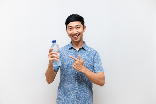 Asian man cheerful smile point finger at water bottle in his hand isolated