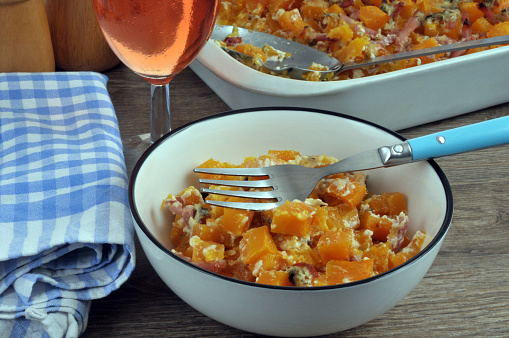 Plate of butternut gratin with diced bacon and a glass of wine