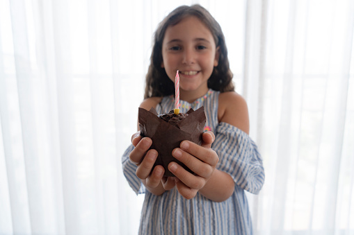 Little girl holding a chocolate muffin with one candle burning