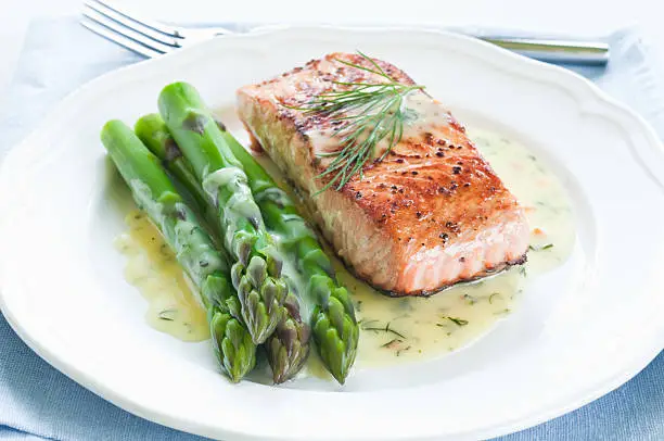 Grilled salmon with asparagus and dill sauce on white plate