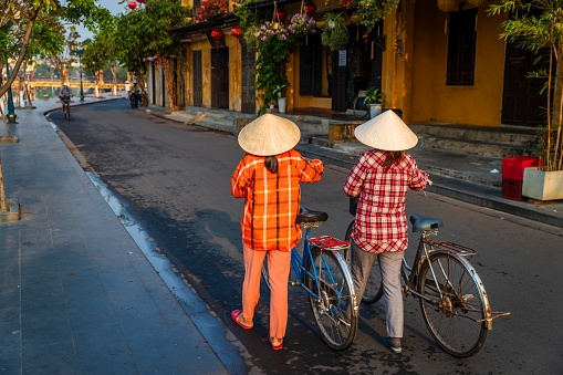 Vietnamese women crossing streets in an old town of Hoi An city, Vietnam. Hoi An is situated on the east coast of Vietnam. Its old town is a UNESCO World Heritage Site because of its historical buildings.