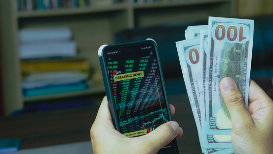 Close up of man counting US Dollars and phone analyzing Crypto Graph at home.