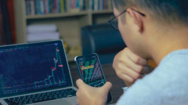 homem asiático usando o telefone analisando crypto graph no laptop em casa. - pension finance retirement graph - fotografias e filmes do acervo