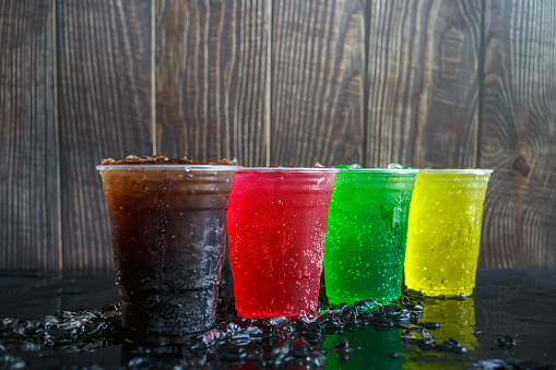 A lot of Soft drinks in colorful and flavorful plastic glasses with ice cubes Chilled on ice on the black background, Soft drinks or Carbonated beverages on ice