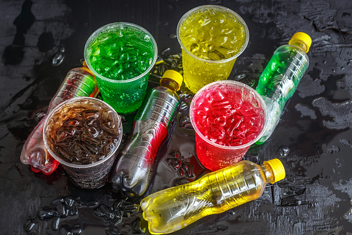Top view A lot of bottles of Soft drinks in colorful and flavorful plastic glasses with ice cubes Chilled on ice on the black background, Soft drinks or Carbonated beverages on ice