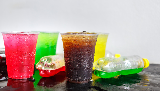 A lot of bottles of Soft drinks in colorful and flavorful plastic glasses with ice cubes Chilled on ice on the black background, Soft drinks or Carbonated beverages