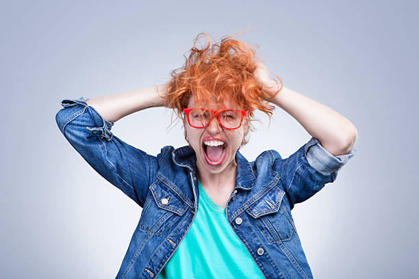 Stressed girl is screaming Woman with red hair holding her head shouting. Stress and hysterical. negative emotions. Studio shot. Gray background hysteria stock pictures, royalty-free photos & images