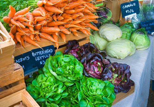 A colorful Vermont farmers market display  shows a variety of locally grown fresh produce including carrots, butterhead lettuce, and cabbage. .