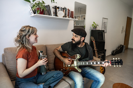 Couple singing song and playing guitar on sofa in living room at home