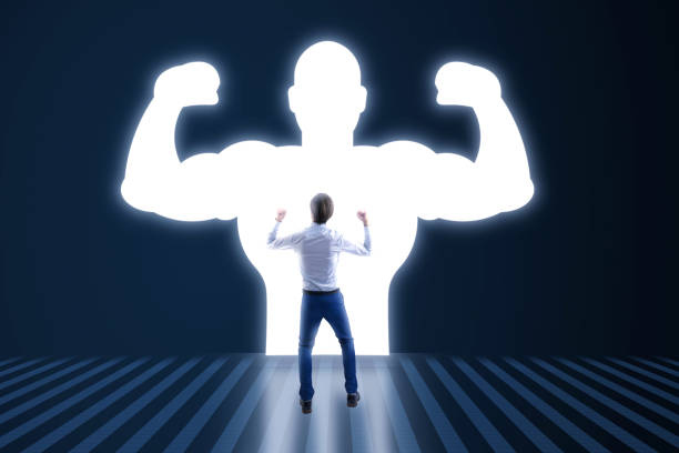 istock Back view of young businessman with very strong illuminated shadow flexing muscles on dark wall background. Personal development, inner strength, motivation concept. 1742631700