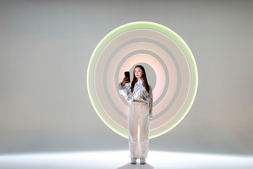 Young woman using a smart phone in front of circular light shape.