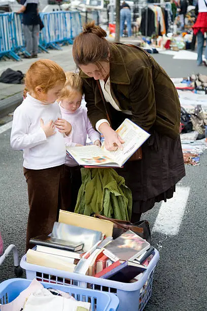 Mother with her daughters, aged 4 and 6, browsing through books at a local flea market.