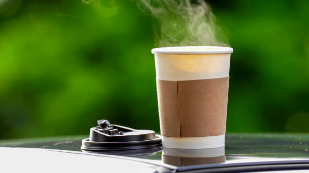 coffee takeaway in a paper cup on top of the car roof green tree background at sunrise in the morning,  selective focus, soft focus. - コーヒー ストックフォトと画像