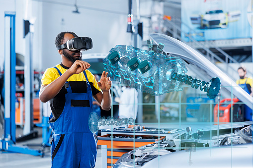 Technician in repair shop using augmented reality holograms to check car performance parameters during maintenance. Licensed garage employee using futuristic vr headset to examine damaged engine