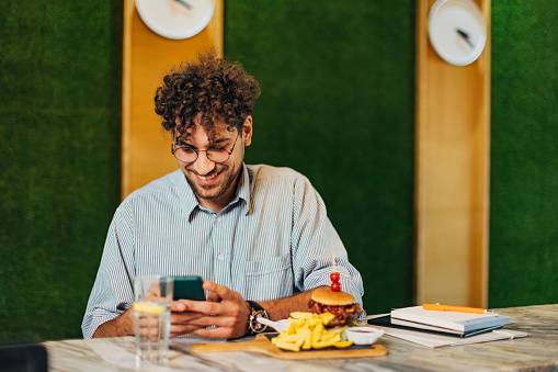 A smiling business man is enjoying his lunch break in a restaurant, using a mobile phone to send text messages