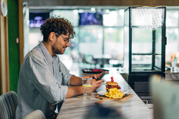 istock Smiling man texting during lunch break in restaurant and eating hamburger 1742678600