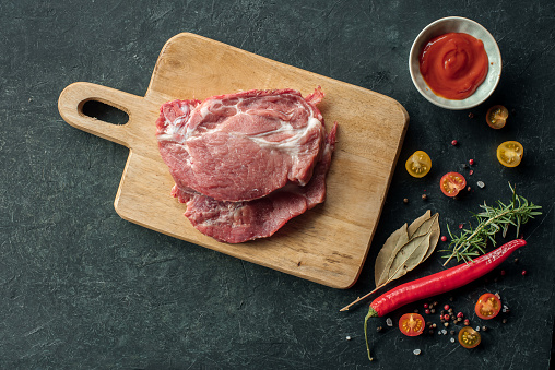 Raw pork meat with spices, hot pepper and tomato sauce for marinating on black background, Top view with place for text