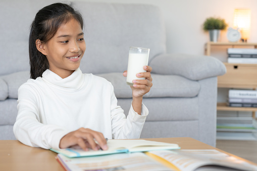 children women drink milk to nourish the body and nourish the brain. asian young little girl learn at home. girl happy drink milk and read a book for exam, Homeschool. education, vitamins, development