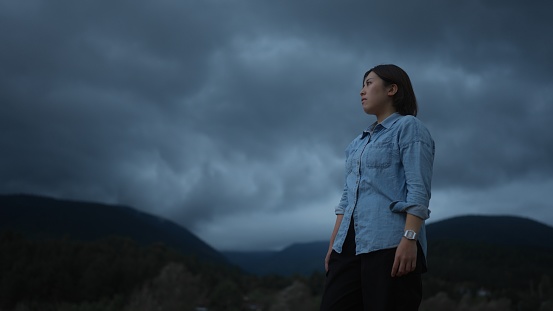 A portrait of a female Asian solo traveler and hiker in a mountain during stormy and windy cold weather.