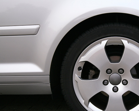 Close-up of the back-end of a silver car with styling strip and alloy wheel (brand names on tire & wheel and serial numbers on tire have been removed)