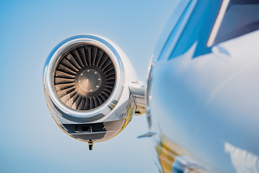 Right side engine of a small business jet. The engine is in focus with a clear blue sky in the background and the fuselage in soft focus in the foreground.
