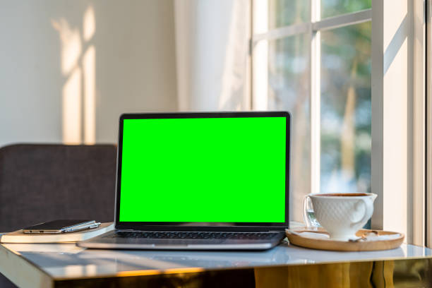 istock Mockup of laptop computer with empty screen with coffee cup and smartphone on table beside the window of the coffee shop background,Green screen 1742714383