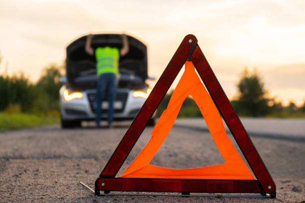 istock Unrecognizable sad driver in reflective vest. Male driver standing near broken car with open up hood. Red triangle to warn other road users of car breakdown or engine failure stop at countryside highway. Emergency traffic 1742715550