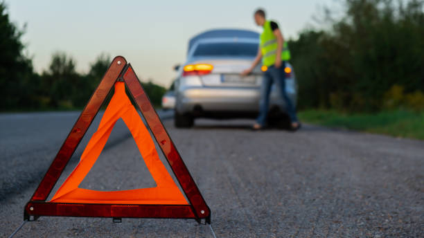 istock Broken silver luxury car emergency accident. Man driver installing red triangle stop sign on road. Sport automobile turned on blinkers technical problems on the road. Safety procedure vehicle broken down 1742717523