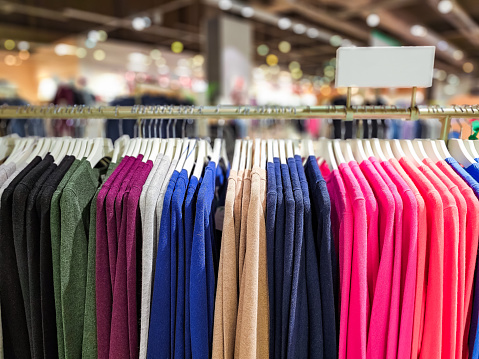 A selection of colorful women's sweaters hanging in a row in the store. Focus on the clothing with the store defocused in the background.