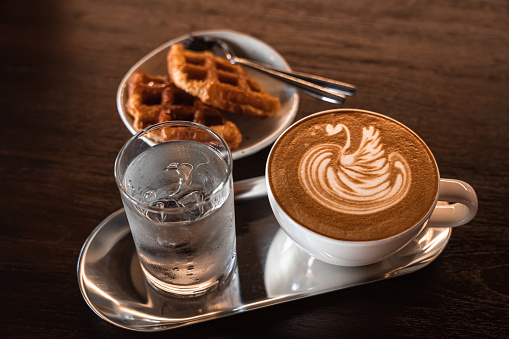 Hot coffee latte with latte art milk foam in a swan shape in cup mug and Homemade Belgian Waffles with honey on wood desk on top view. As breakfast In a coffee shop at the cafe,during business work.