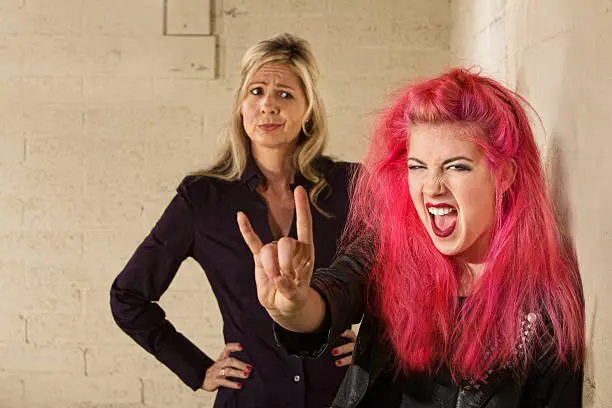 Teenager in pink hair with disapproving mother in background