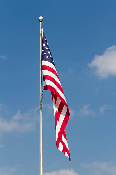 US Flag on Pole with Blue Sky The flag of the United States of America flies from a flagpole in this vertical orented photograph with great detail and vibrant colors. flagpole stock pictures, royalty-free photos & images