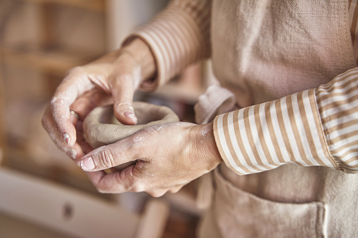 Close-up view of the hands of a female artisan molding a piece of ceramic.