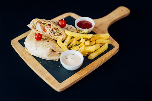 Delicious wrap sandwich served on a wooden cutting board with two sauces on the side and a cherry tomato garnish