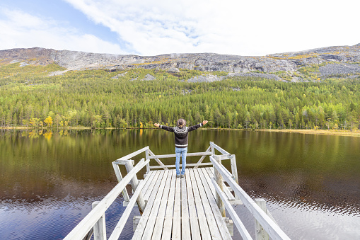 Man enjoying peaceful environment in Norway. Lake and green mountains.
He relaxes on a wooden pier.
