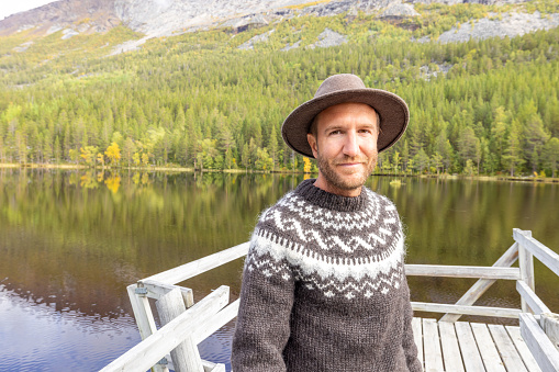 Man enjoying peaceful environment in Norway. Lake and green mountains.
He relaxes on a wooden pier.